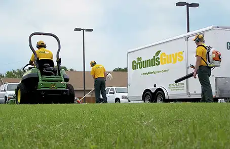Three Grounds Guys associates performing lawn cleanup next to a branded company trailer.