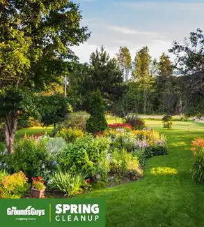Beautifully landscaped, lush backyard with the Grounds Guys logo and the words Spring Cleanup at the bottom.
