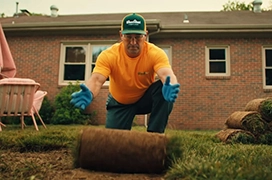 The Grounds Guys service professional installing a roll of sod in a backyard.