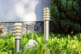 Two steel column light posts installed among plants next to the side of a home.