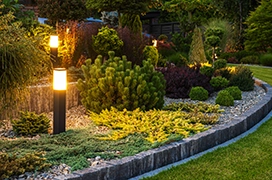 A plant bed with a variety of shrubs and plants accented by column lights and framed by stone blocks.