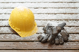 Light snow covering a yellow hard hat, pair of gloves, and the surface of a deck.