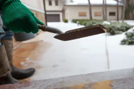 A gloved hand holding a trowel with sand and spreading it over a walkway.