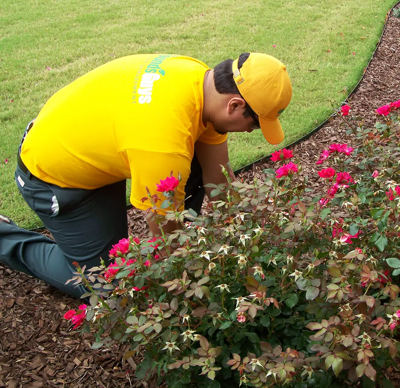 The Grounds Guys service professional tending to a colorful flower bed with brown mulch.