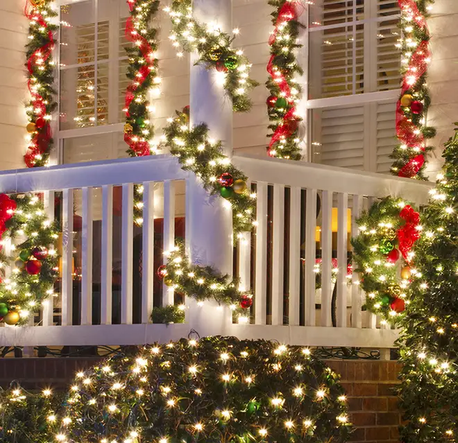 White holiday lights and garland decorating a front porch.