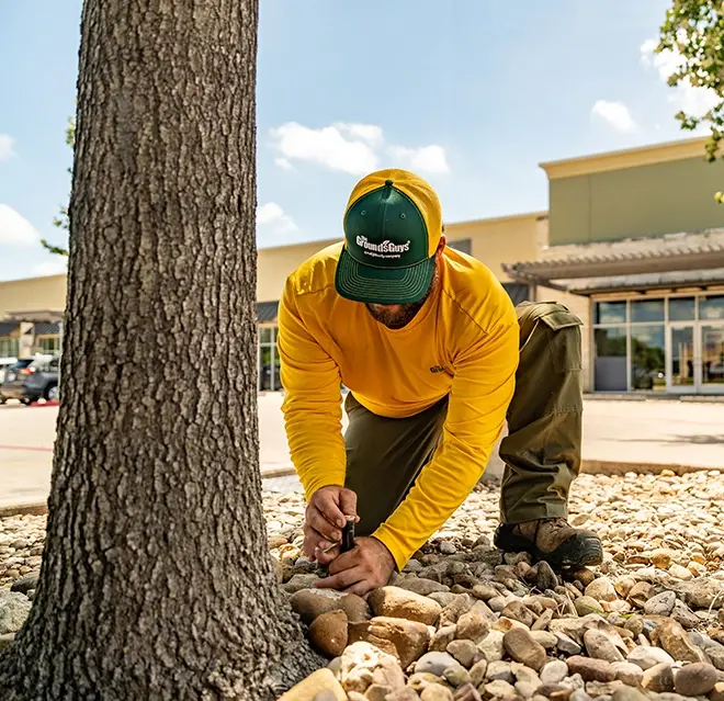 The Grounds Guys service professional adjusting a sprinkler head in a rock bed at a retail property.
