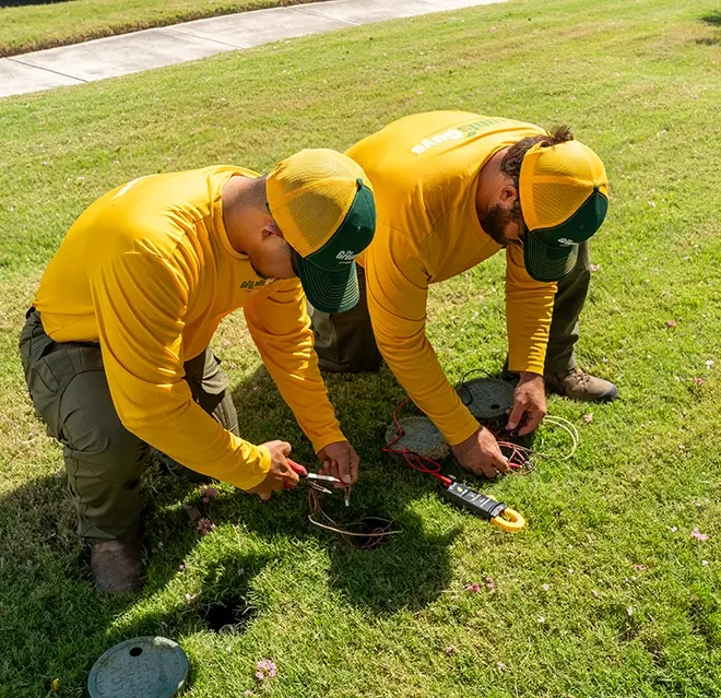 Two Grounds Guys service professionals installing part of a smart sprinkler system in the grass.