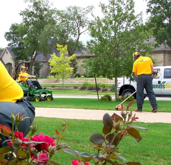 The Grounds Guys service professionals mowing and edging a lawn.