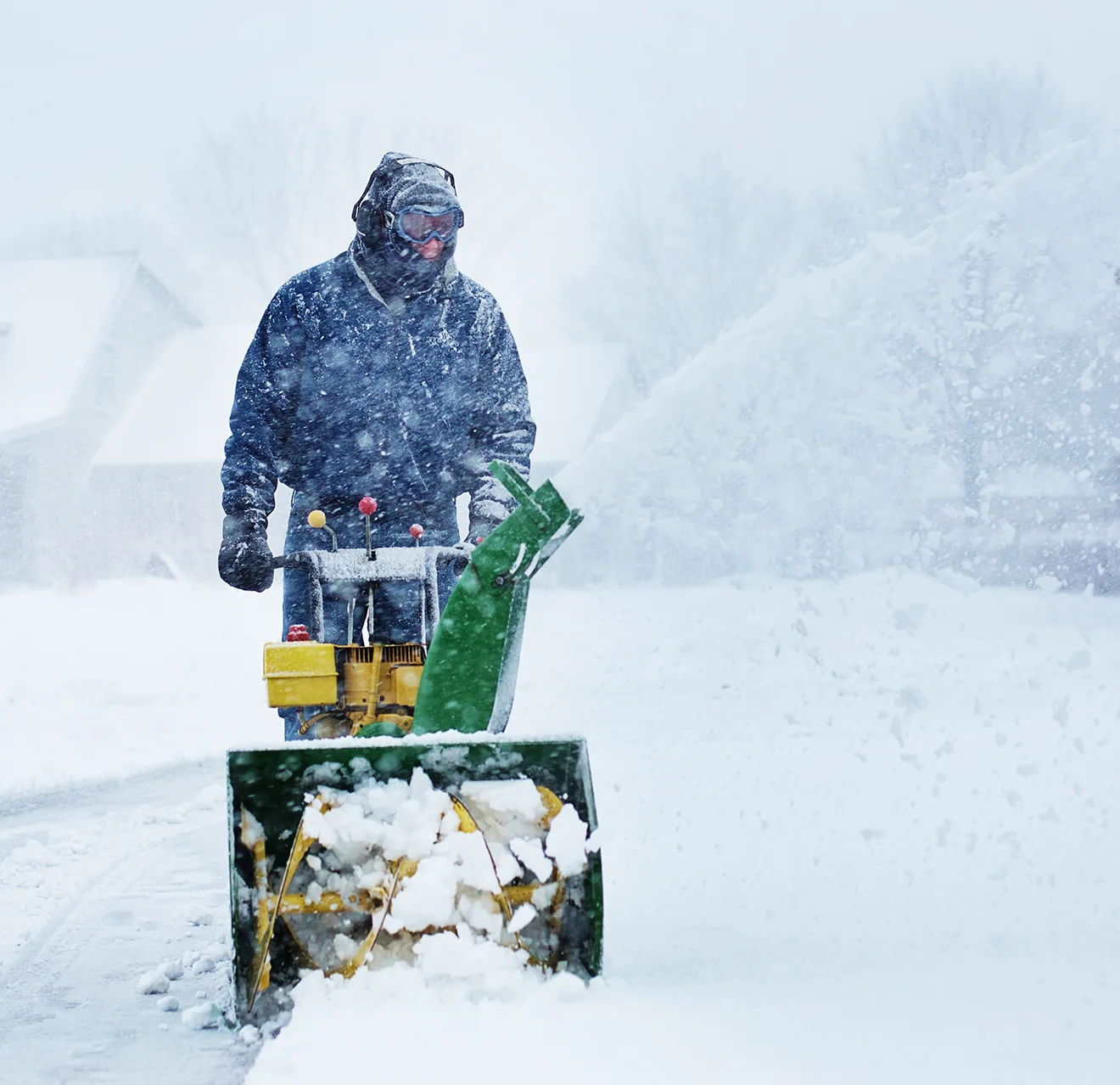 Man in snow gear using snow blower.