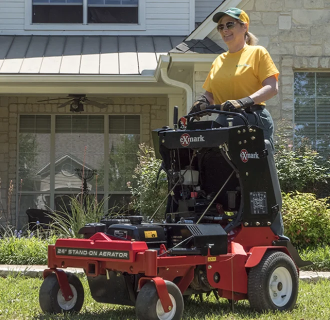 The Grounds Guys service professional aerating a home's front lawn on a stand-on aerator.