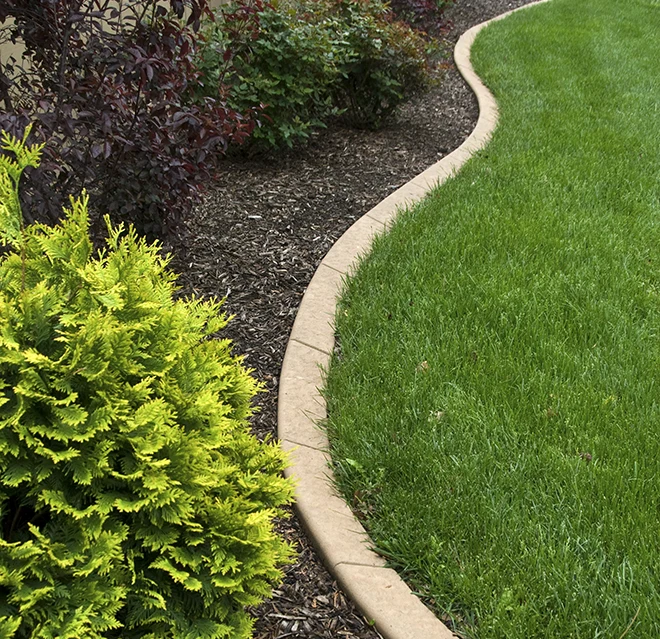 A concrete landscape curb framing a brown-mulch plant bed, next to a vibrant green lawn.