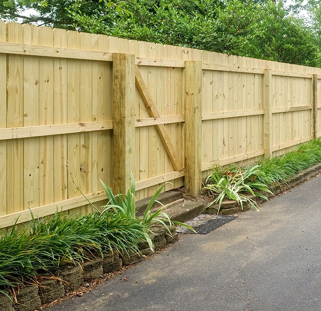 A natural-wood fence with a row of hostas along it.