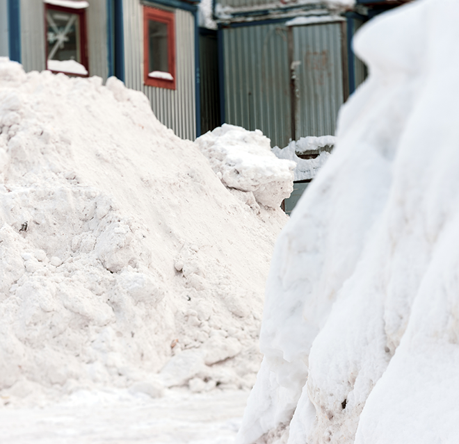 Snow piled high on the sides of a walkway outside an office building.