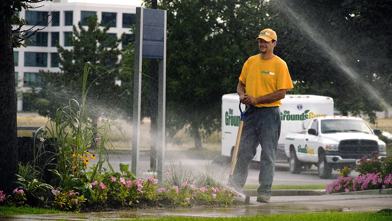 The Grounds Guys service professional monitoring sprinklers as they spray water on a lawn.