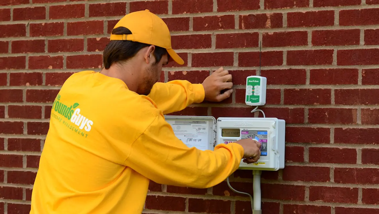 The Grounds Guys service professional adjusting a smart timer on the exterior of a building.