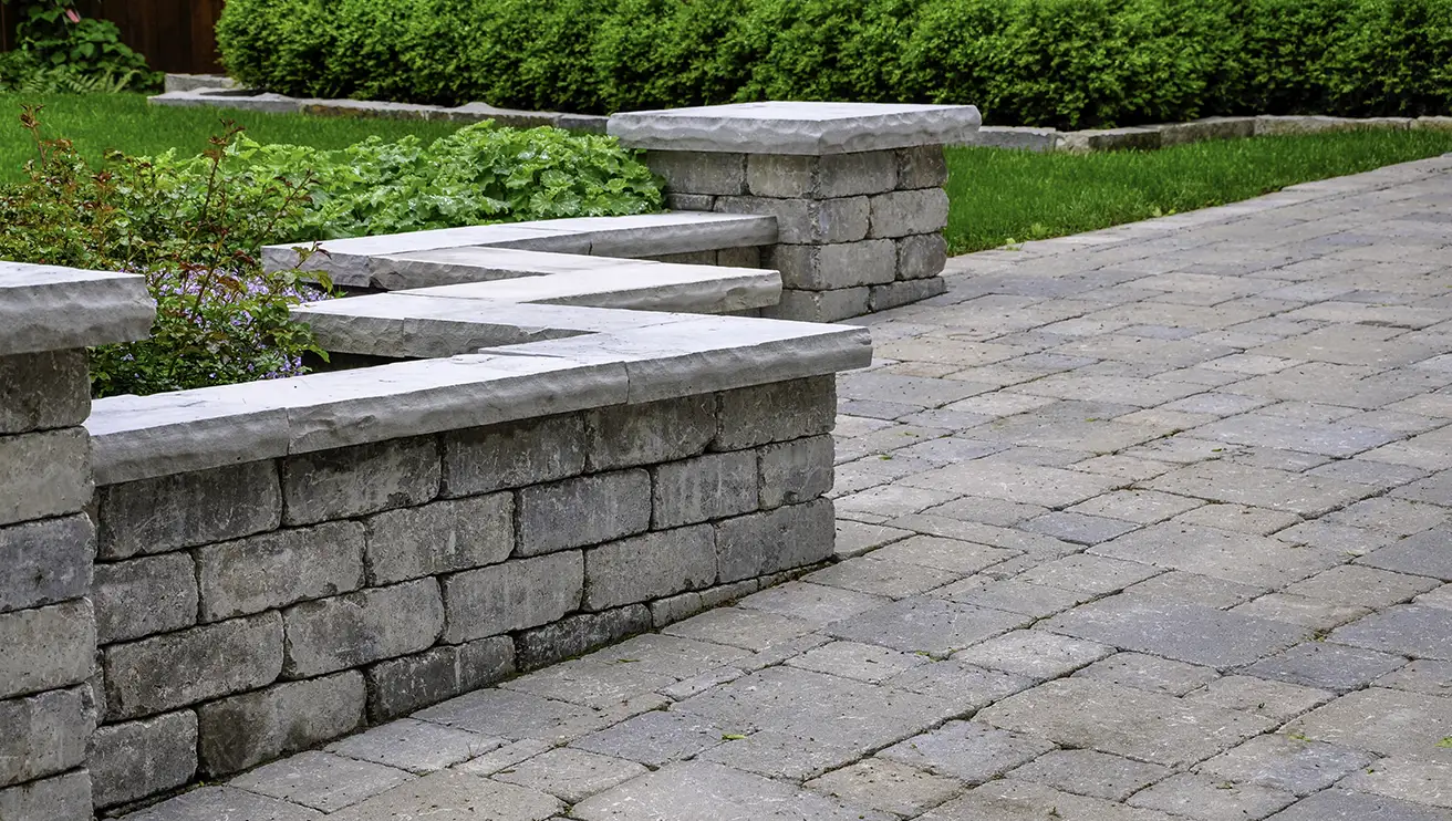 A low stone wall with plant beds built along the edge of a stone patio.