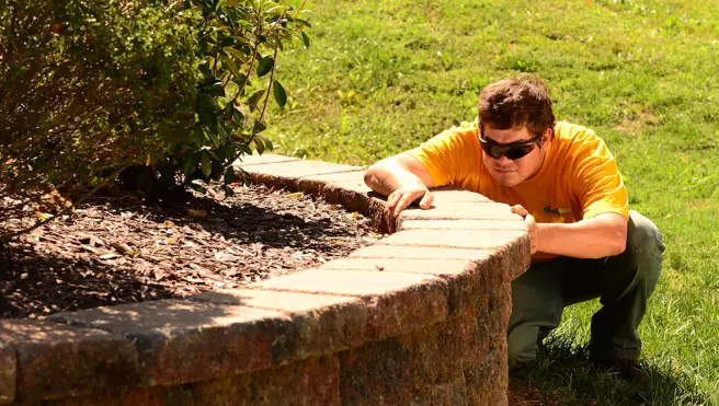 The Grounds Guys service professional adjusting a stone paver in a raised garden bed.