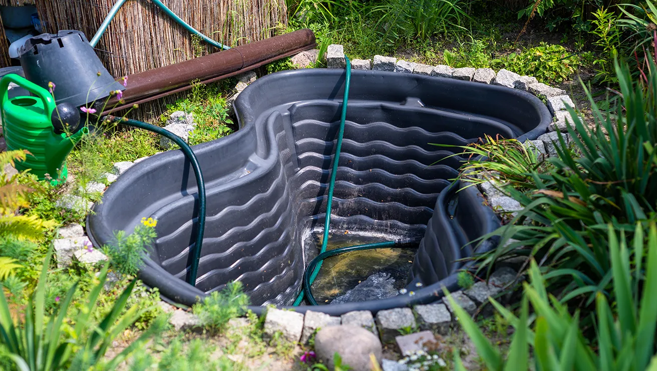 Empty plastic garden water tank into the ground with water hose into it.