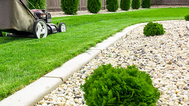 A concrete landscape edge framing a rock bed, with lush green grass being mowed next to it.