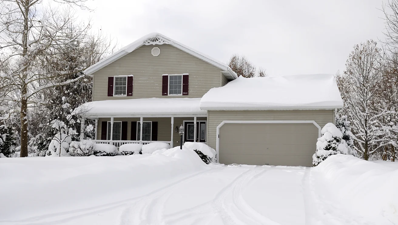 A snow-covered home and lawn, with its driveway cleared of snow.