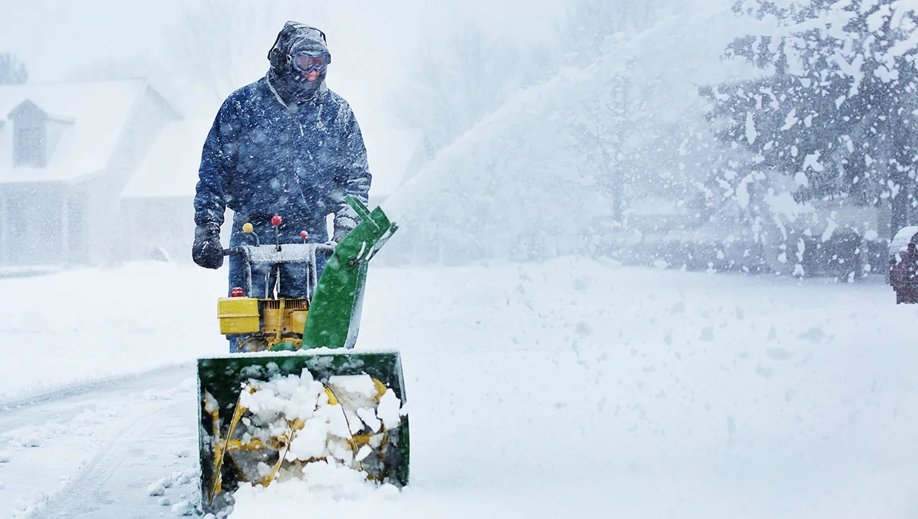 The Grounds Guys service professional using a snow blower during a snowstorm.