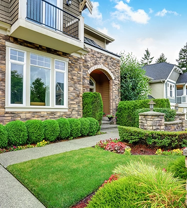 A home's front yard with trimmed shrubs, flowers, and low stone walls.