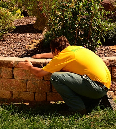 The Grounds Guys service professional adjusting a stone in a garden bed retaining wall.