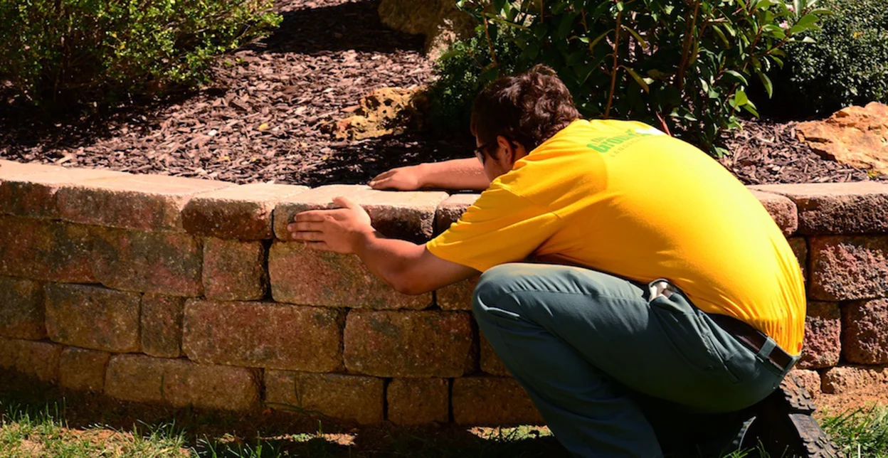 The Grounds Guys service professional adjusting a stone in the retaining wall of a raised bed.