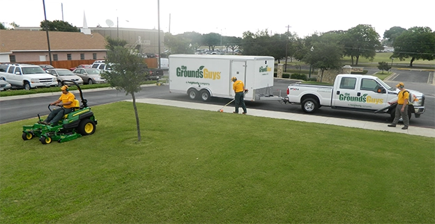 The Grounds Guys team mowing and edging a commercial property's lawn.