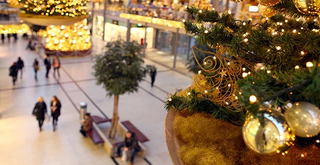 Holiday lighting and decorations hung from the upper story of a mall, with shoppers visible below.