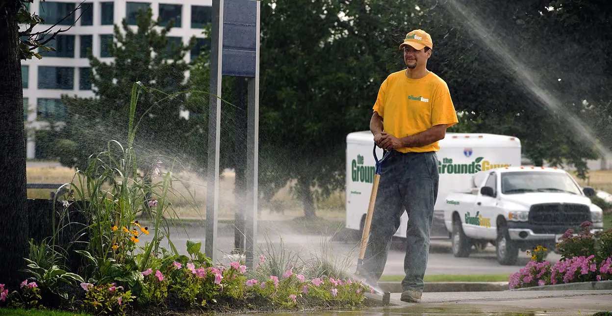 The Grounds Guys service professional watching water spray from sprinkler heads installed in a lawn.