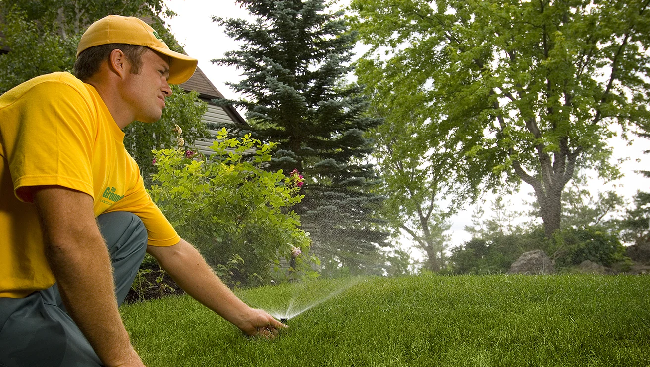 The Grounds Guys service professional adjusting a sprinkler head in the grass as it sprays water.