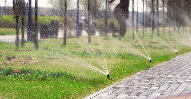 A row of sprinkler heads spraying water on a commercial property's lawn.