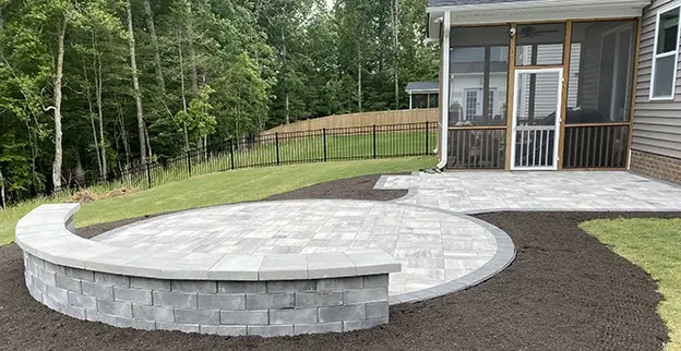 A circular stone patio with a low accent wall in the backyard of a home.