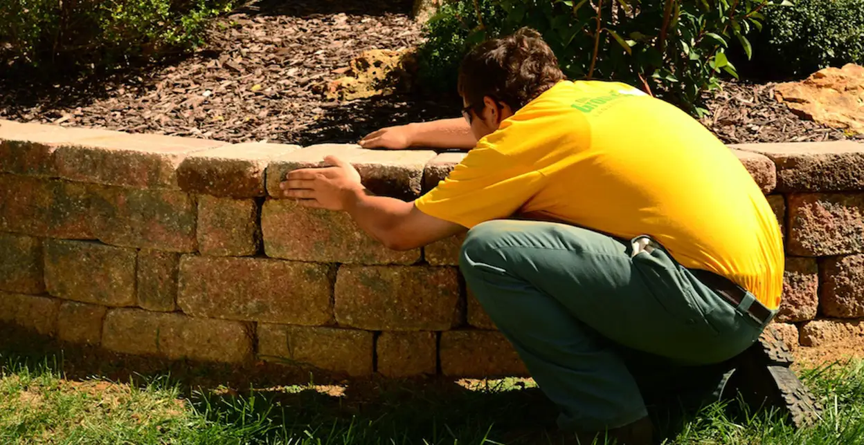 The Grounds Guys service professional adjusting a stone in a raised garden bed.