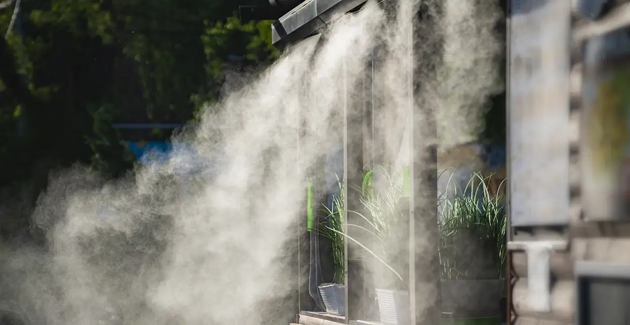 A misting system spraying mists of water onto plants on a patio.