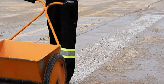 The Grounds Guys service professional using a salt spreader to apply salt to a road.