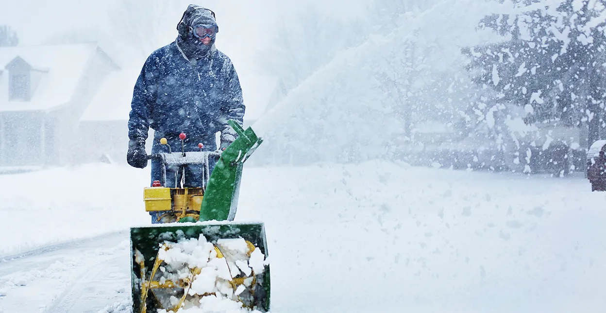 The Grounds Guys service professional using a snow blower during a snowstorm.