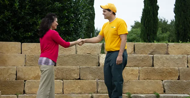 The Grounds Guys service professional shaking hands with a customer next to shrubs and stone steps.