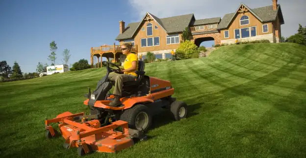 The Grounds Guys service professional mowing a large home's front lawn.