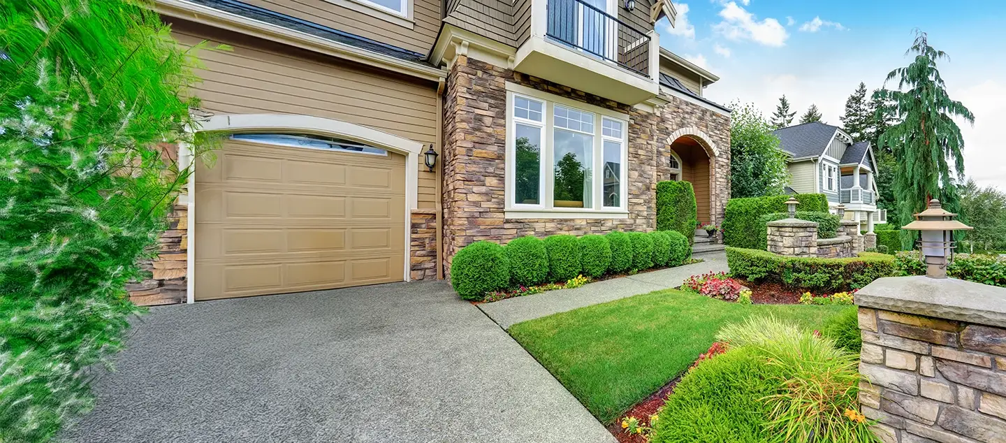 A home's front yard with trimmed shrubs, flowers, and low stone walls.