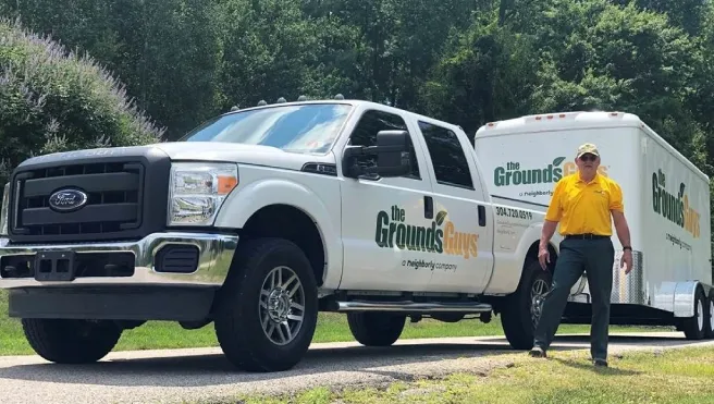 The Grounds Guys of Charleston, WV, owner Greg Paxton in front of branded truck and trailer.