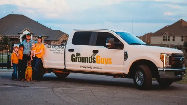 The Grounds Guys of Little Elm owners Ben and Alison Vance with family next to branded truck.