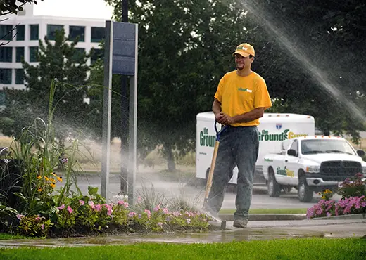 The Grounds Guys service professional adjusting a sprinkler head in the grass as it sprays water.