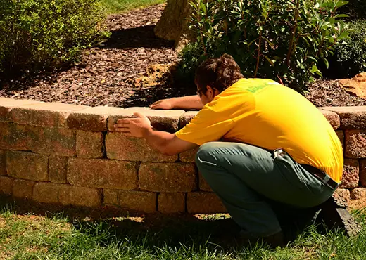 The Grounds Guys service professional adjusting a stone in a raised garden bed.