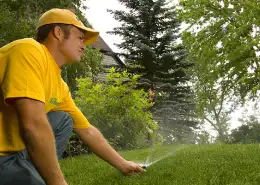 The Grounds Guys service professional adjusting a sprinkler head in the grass as it sprays water. 