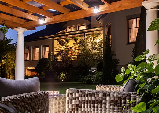 A backyard patio with pergola lit by outdoor lighting. 