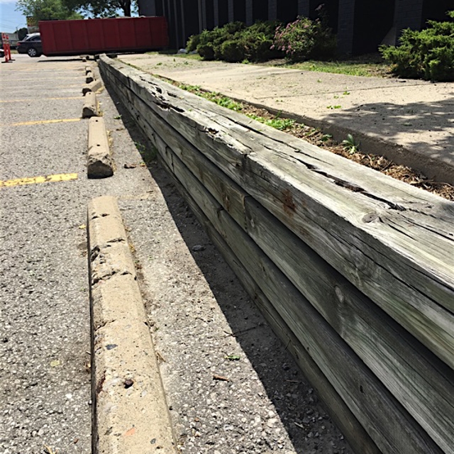 A Car parking a wooden plank border with stone pavement on the side.