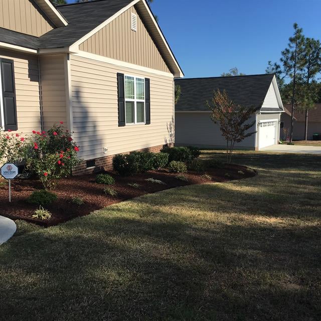 A nicely cut garden with a porch in the background.