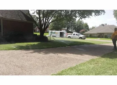 Driveway lined by green grass with sprinklers with the Grounds Guys Truck on the street